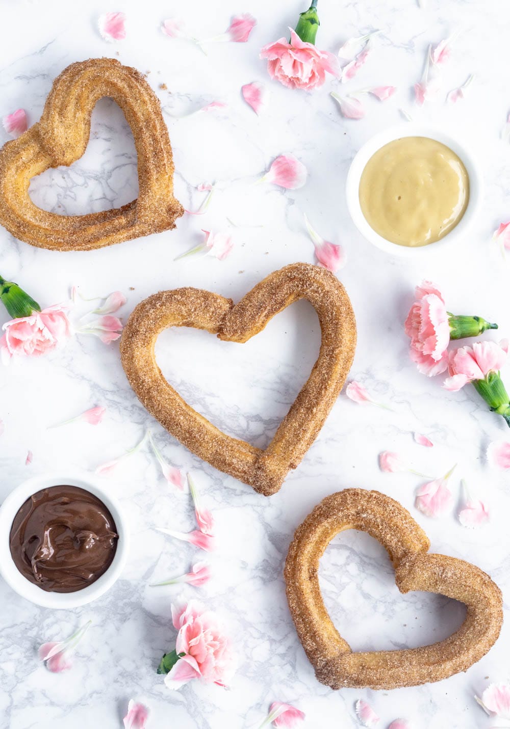 3 heart shaped churros on a marble background with pink flowers