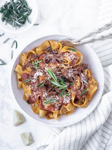 pappardelle with beef short rib ragu in a plate topped with rosemary