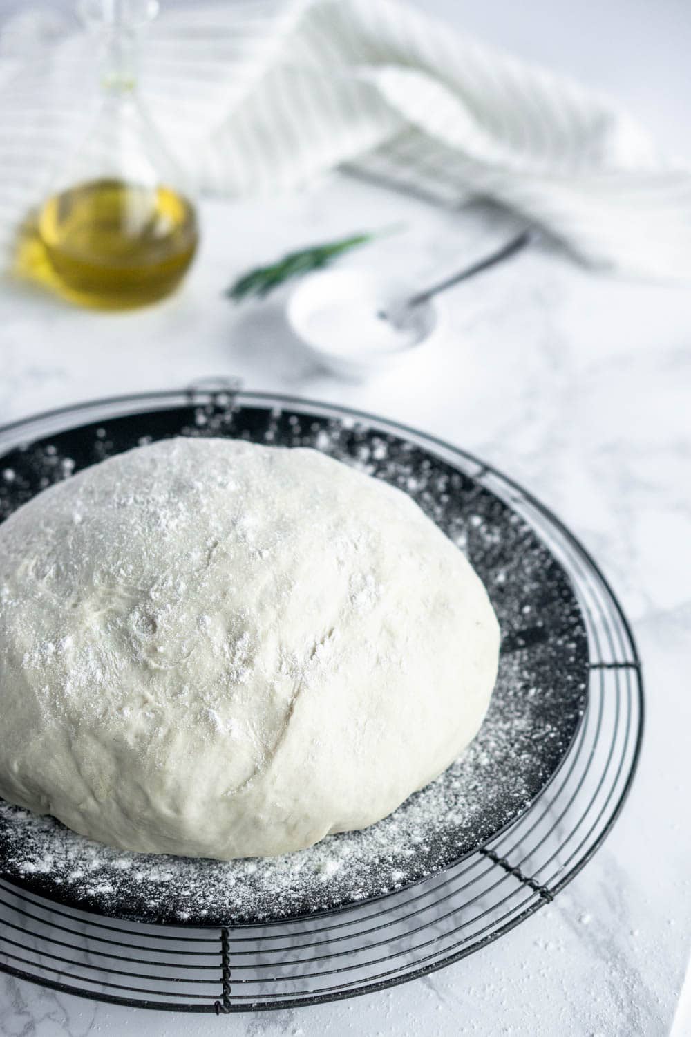 pizza dough on a black plate with olive oil and rosemary in the background
