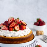 olive oil cake topped with mascarpone cream and sliced prosecco strawberries, and a bowl of strawberries in the background