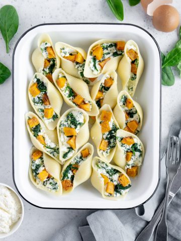 Stuffed Pasta Shells in a white pan surrounded by spinach and fresh ricotta