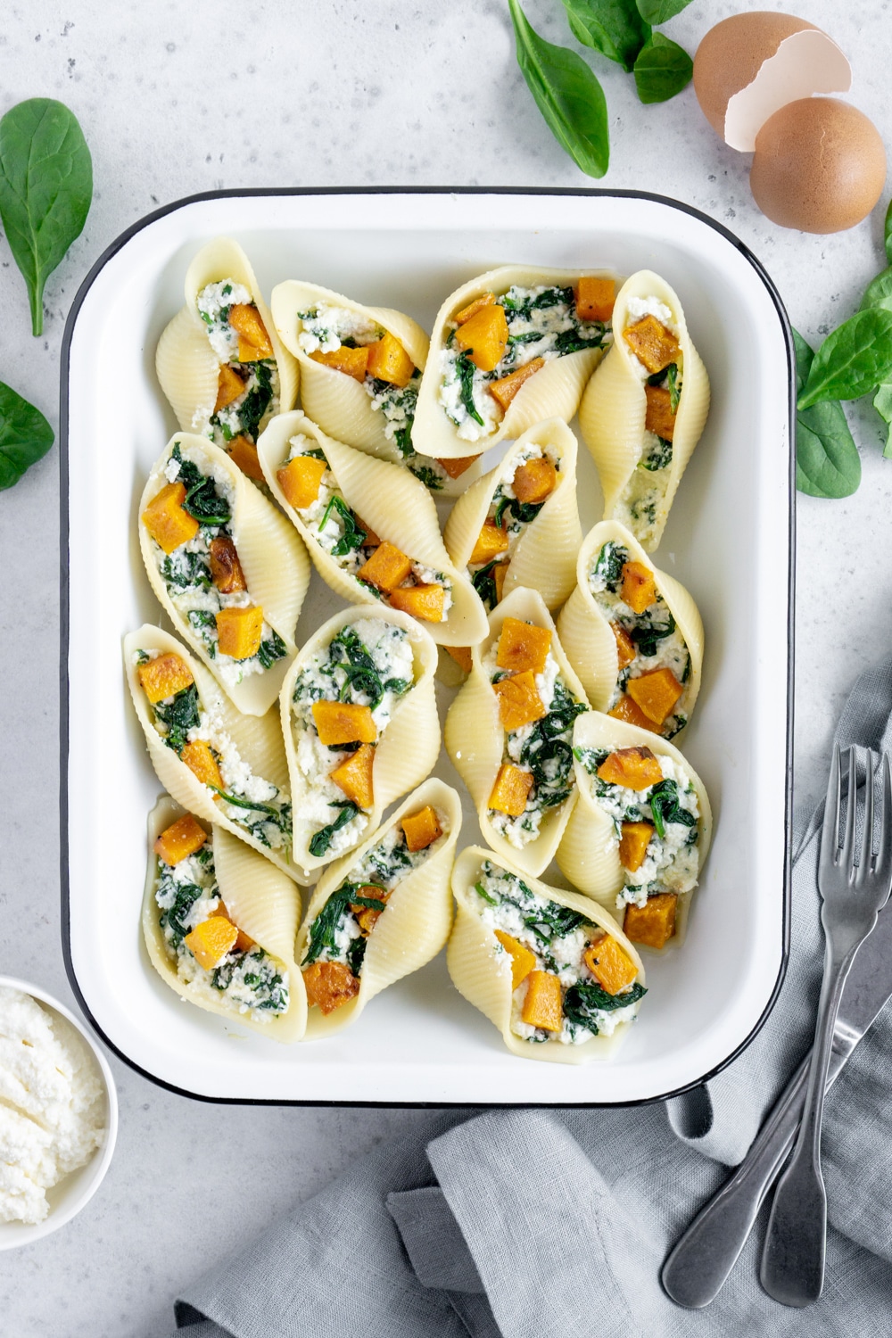 Stuffed Pasta Shells in a white pan surrounded by spinach and fresh ricotta