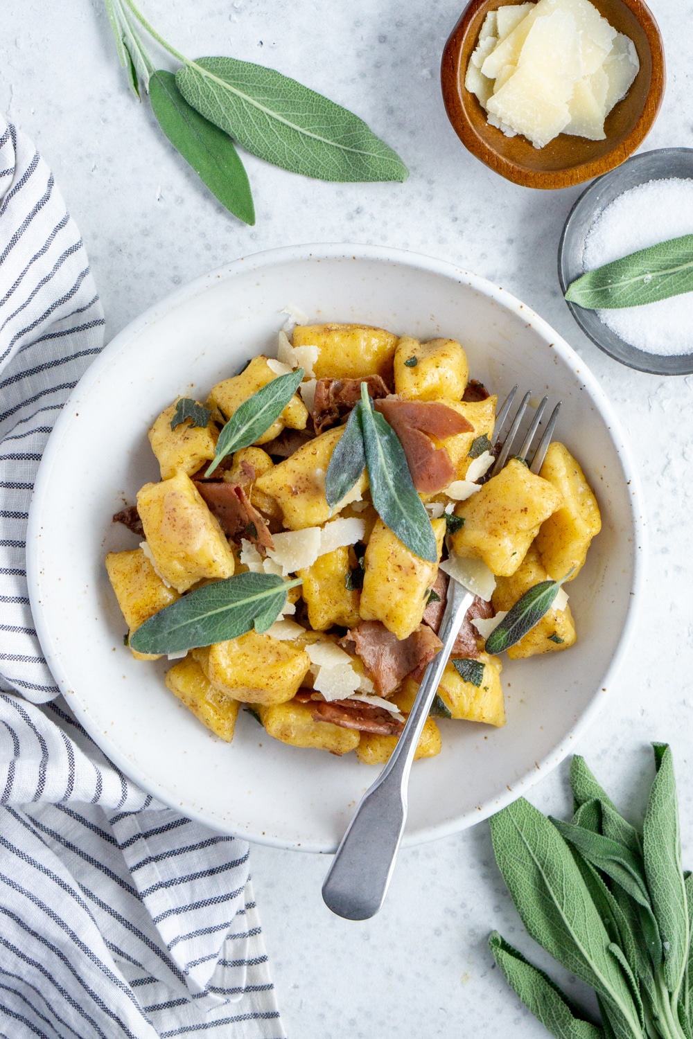 Bowl of butternut squash gnocchi topped with sage and bowls of salt and cheese to the side
