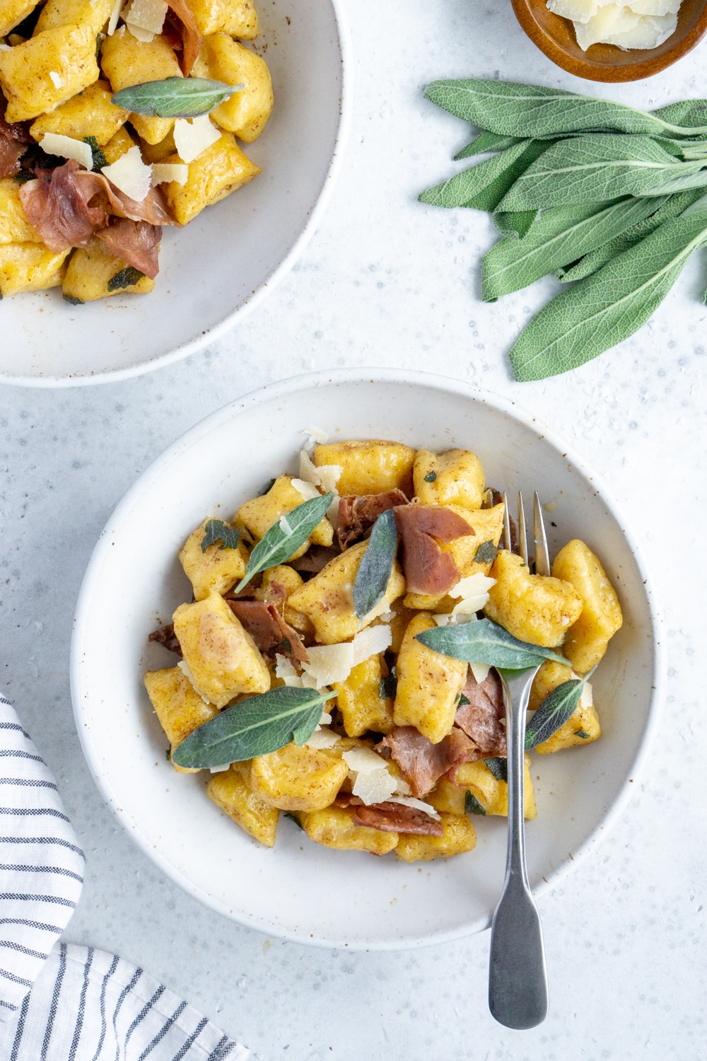 Two bowls of butternut squash gnocchi with a bunch of sage