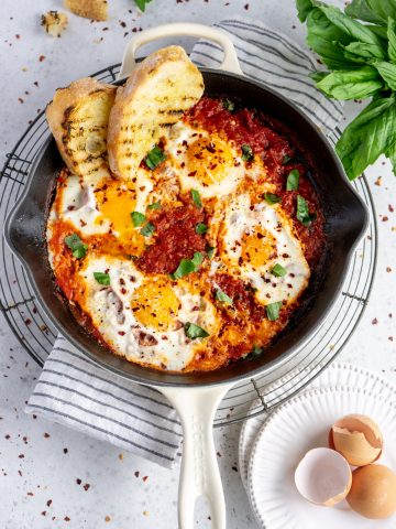 Eggs in purgatory in a white pan and grilled bread in the pan