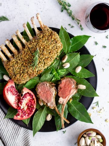 two lamb chops on a plate with a whole rack of lamb on a bed of bay leaves
