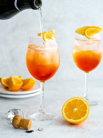 2 glasses of aperol spritz with prosecco being poured into one glass