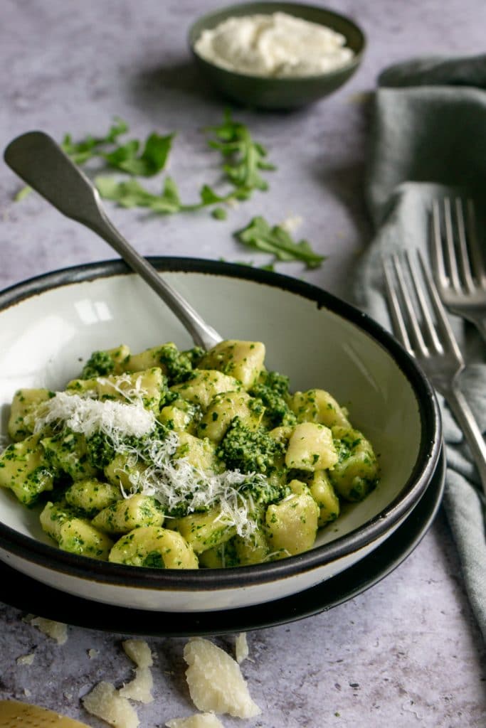 Side view of a bowl of ricotta gnocchi with a small dish of ricotta in the background