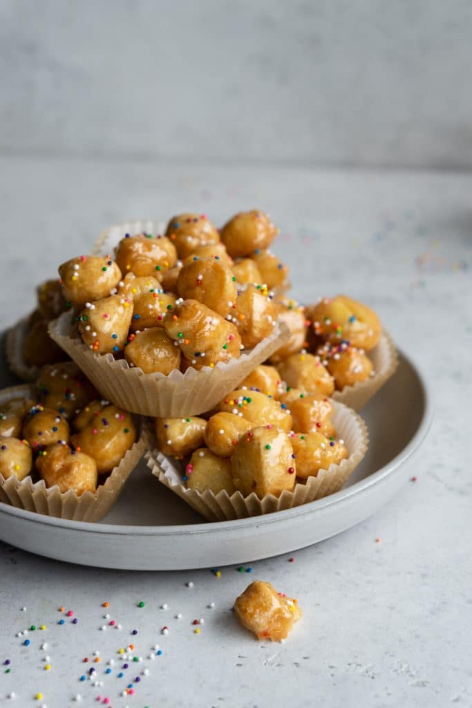 Authentic struffoli topped with sprinkles in muffin liners in a plate