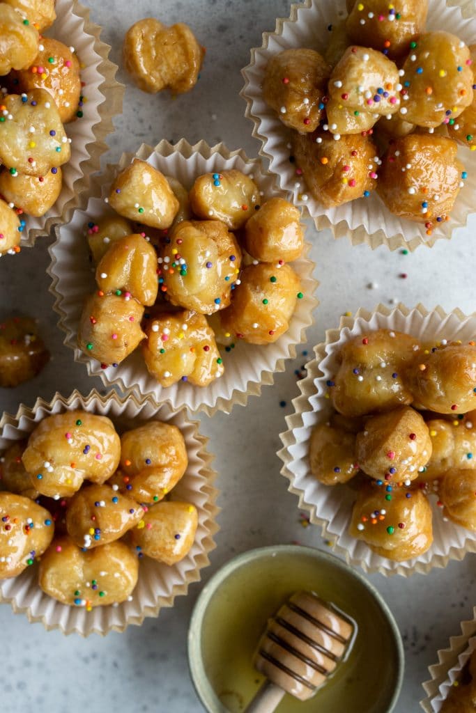 Overhead shot of struffoli in muffin liners with a dish of honey