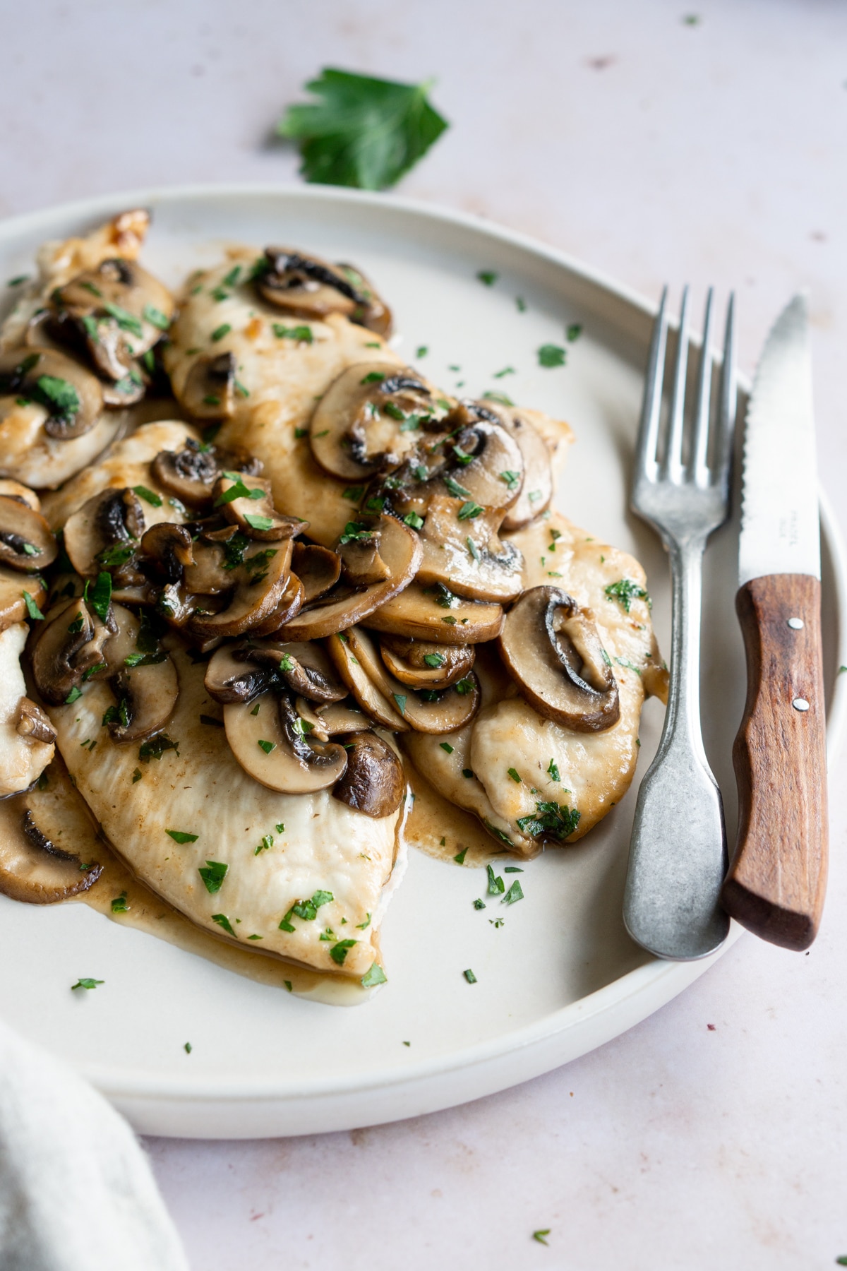Mushroom chicken in a plate topped with parsley and a fork and knife
