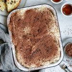 panettone tiramisu in a baking dish with a napkin to the side, and two espressos