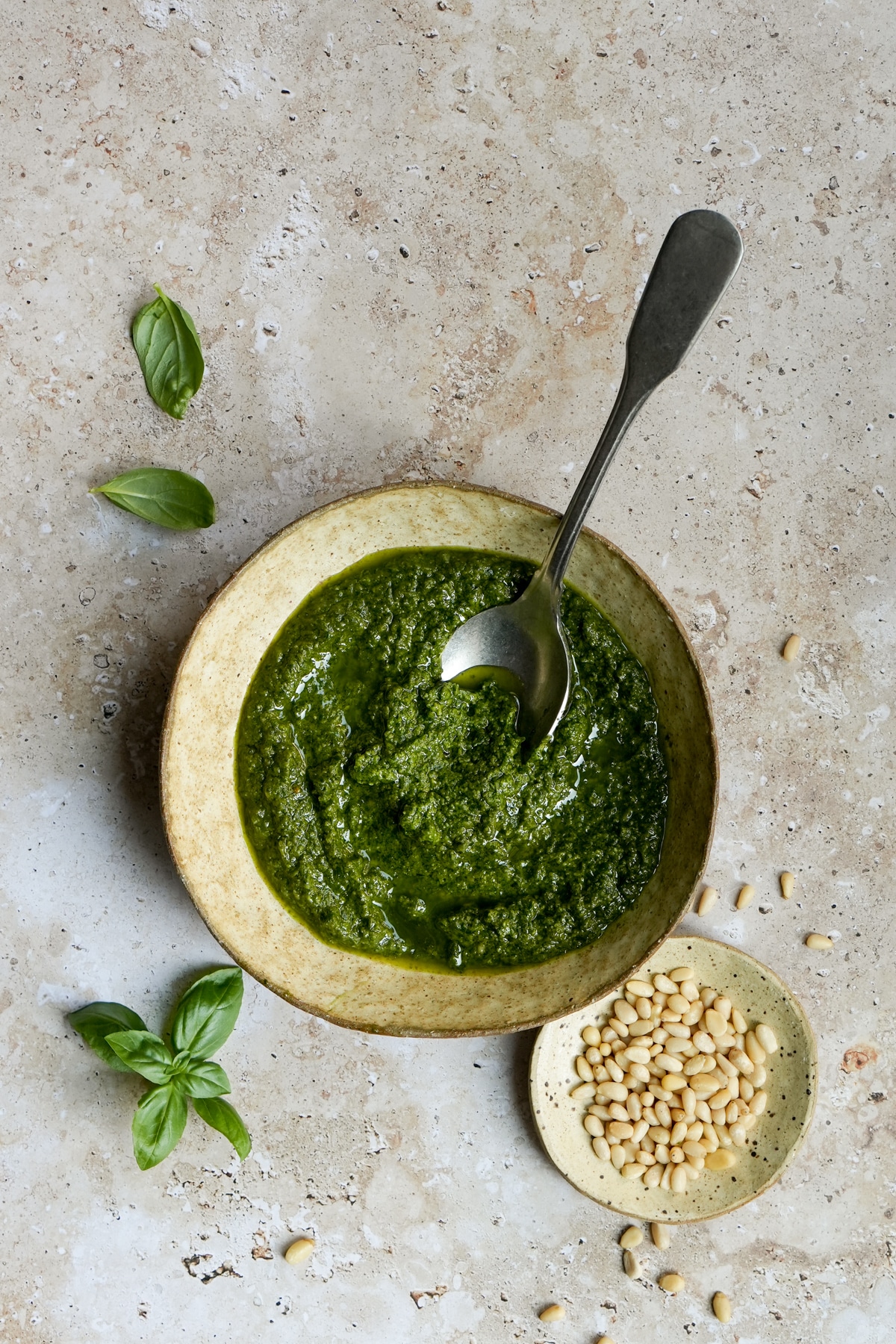Pesto genovese in a bowl with a small dish of pine nuts to the side