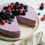 Berry mousse cake topped with fresh berries on a plate with a slice cut out