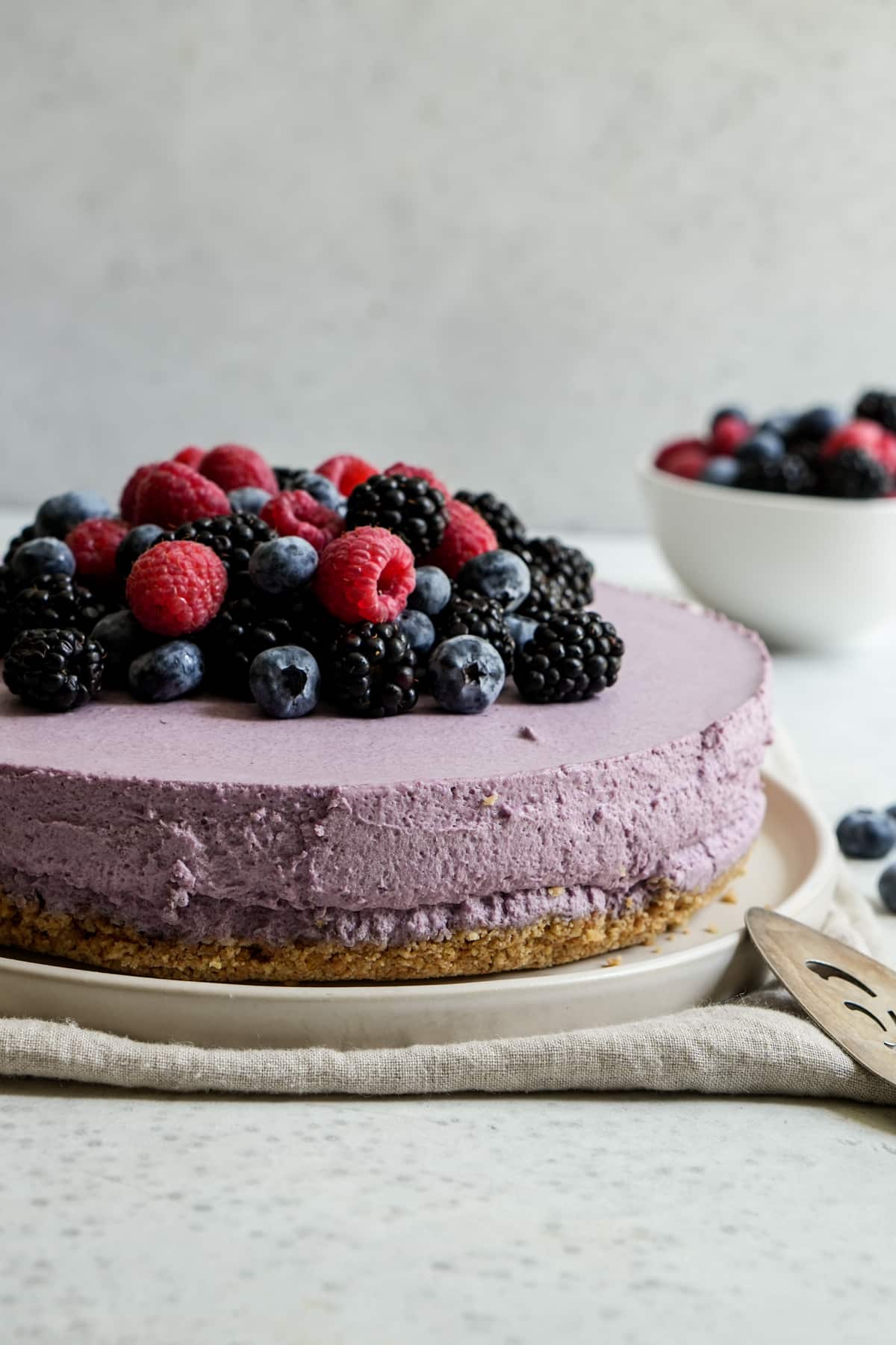 Berry mousse cake in a plate with a bowl of fresh berries in the background