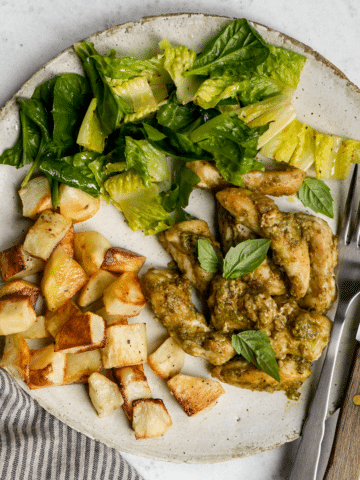 Pesto chicken in a plate with roasted potatoes and salad