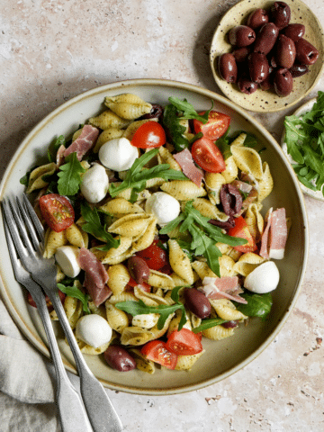 Arugula pasta salad in a bowl with a small plate of olives to the side