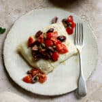 Italian halibut with tomatoes, olives and capers in a plate with a fork