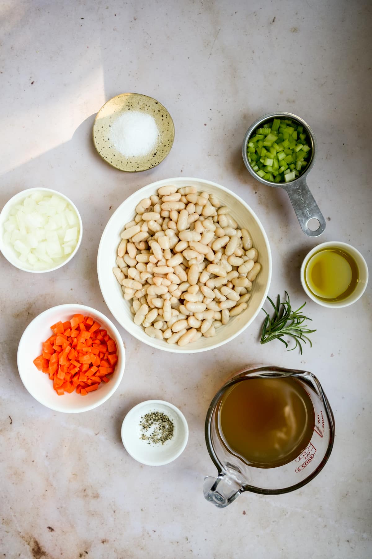 Italian white bean soup ingredients - cannellini beans, chopped celery, carrot, onion, olive oil, rosemary, vegetable stock, salt and pepper