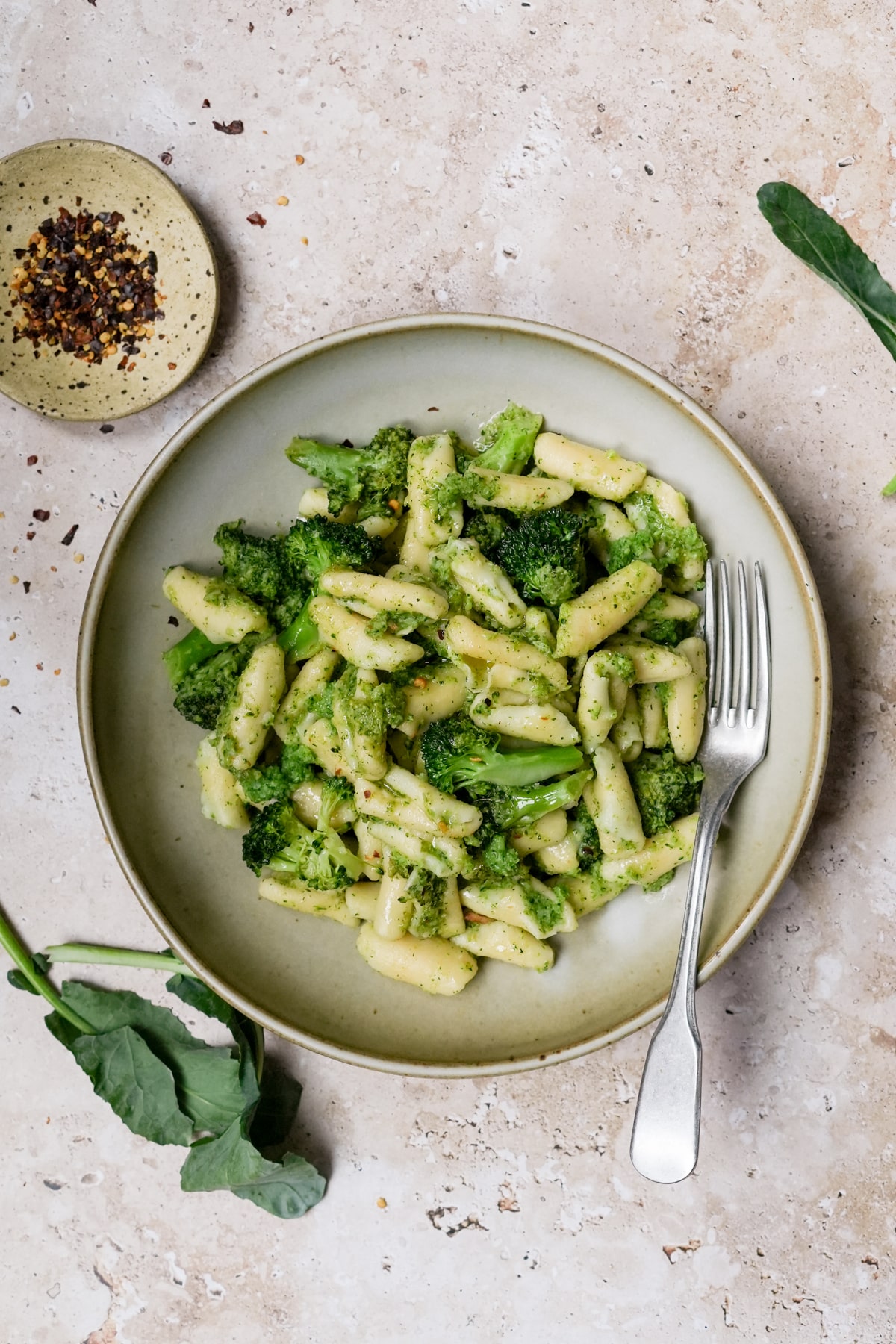Cavatelli and broccoli in a bowl surrounded by broccoli leaves