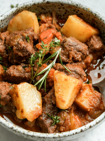 Bowl of Italian beef stew (spezzatino) topped with fresh rosemary and thyme