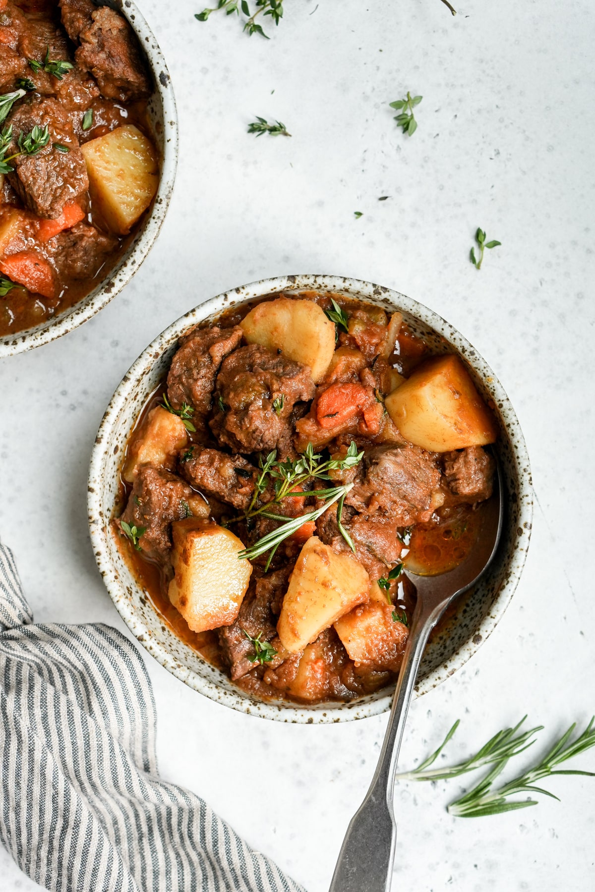 Two bowls of Italian beef stew (spezzatino) with fresh herbs scattered around