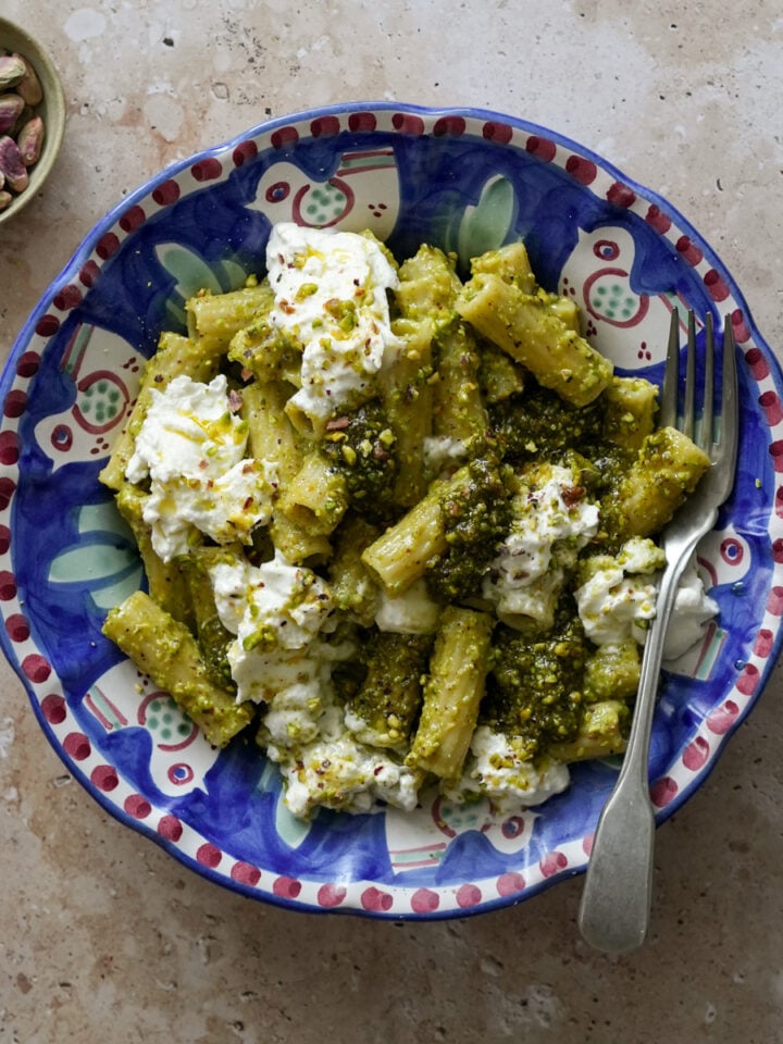 Italian pistachio pasta in a bowl topped with burrata with a small bowl of pistachios to the side