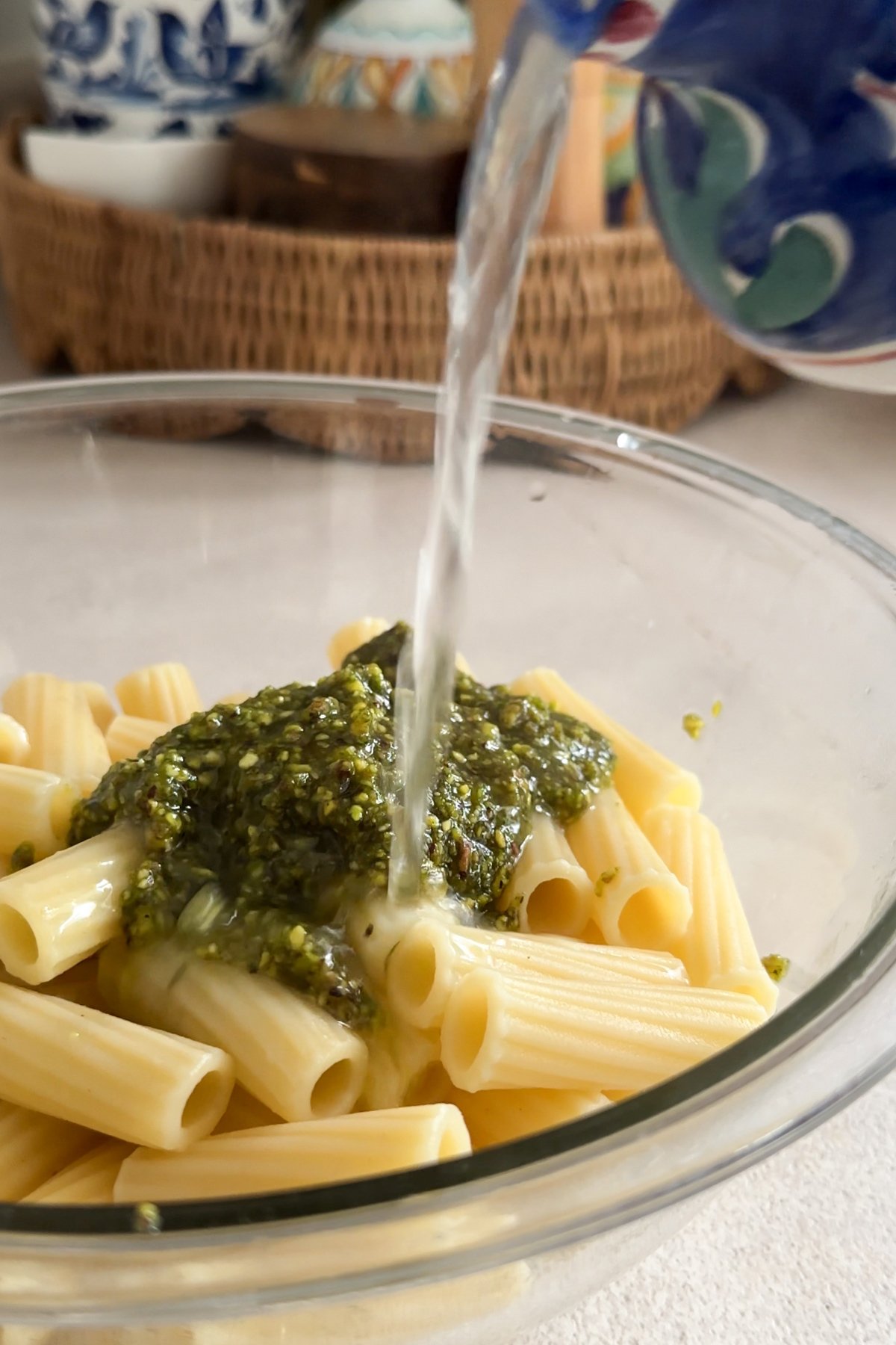 Pasta water being poured into bowl with pasta and pistachio pesto in it
