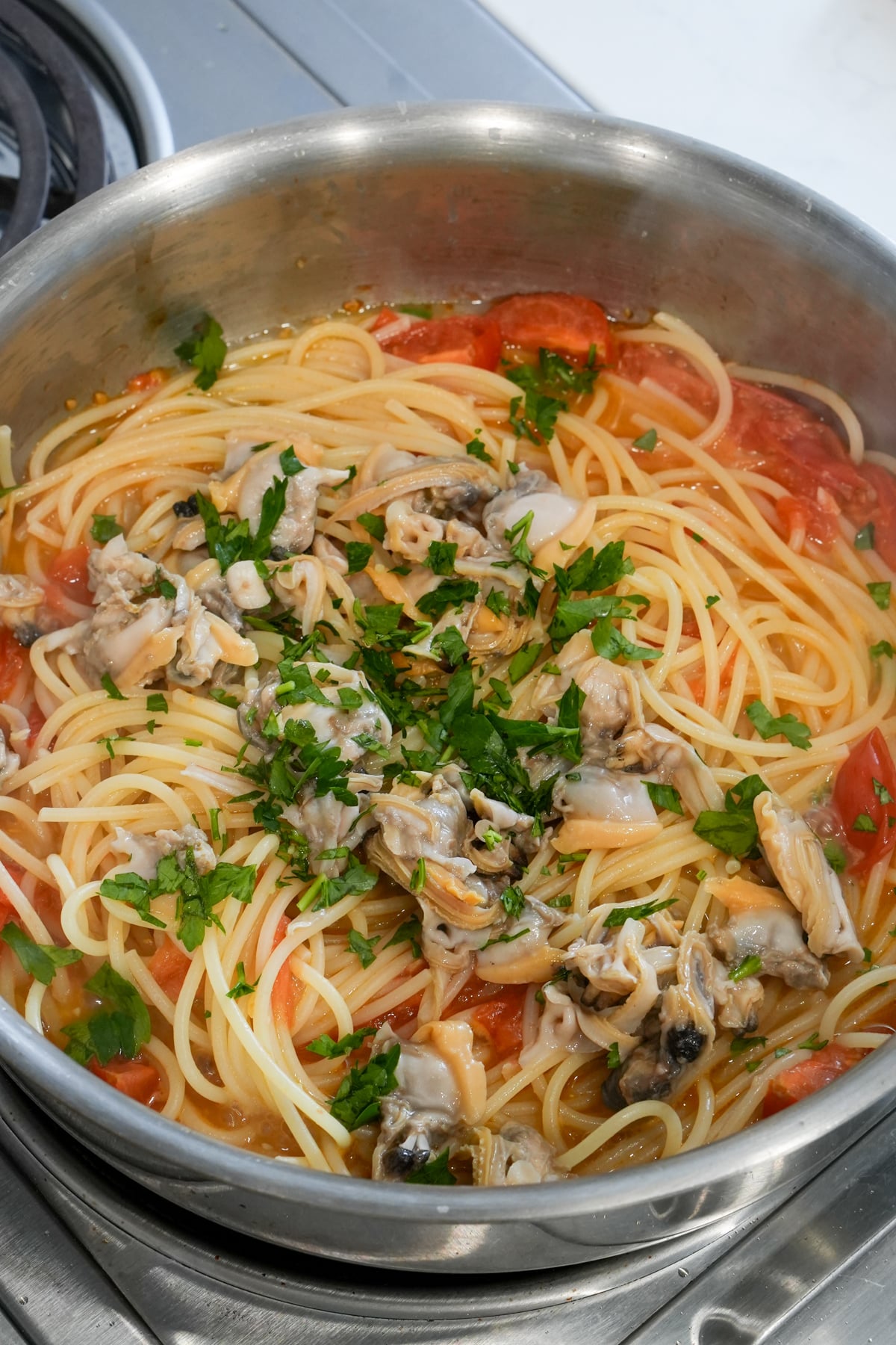 spaghetti in a pan, with clams and minced parsley on top