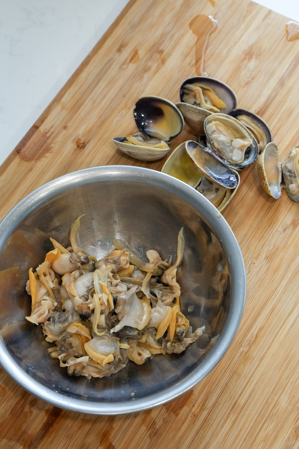 clams removed from shell in a bowl, with unshelled clams next to them on a wooden board