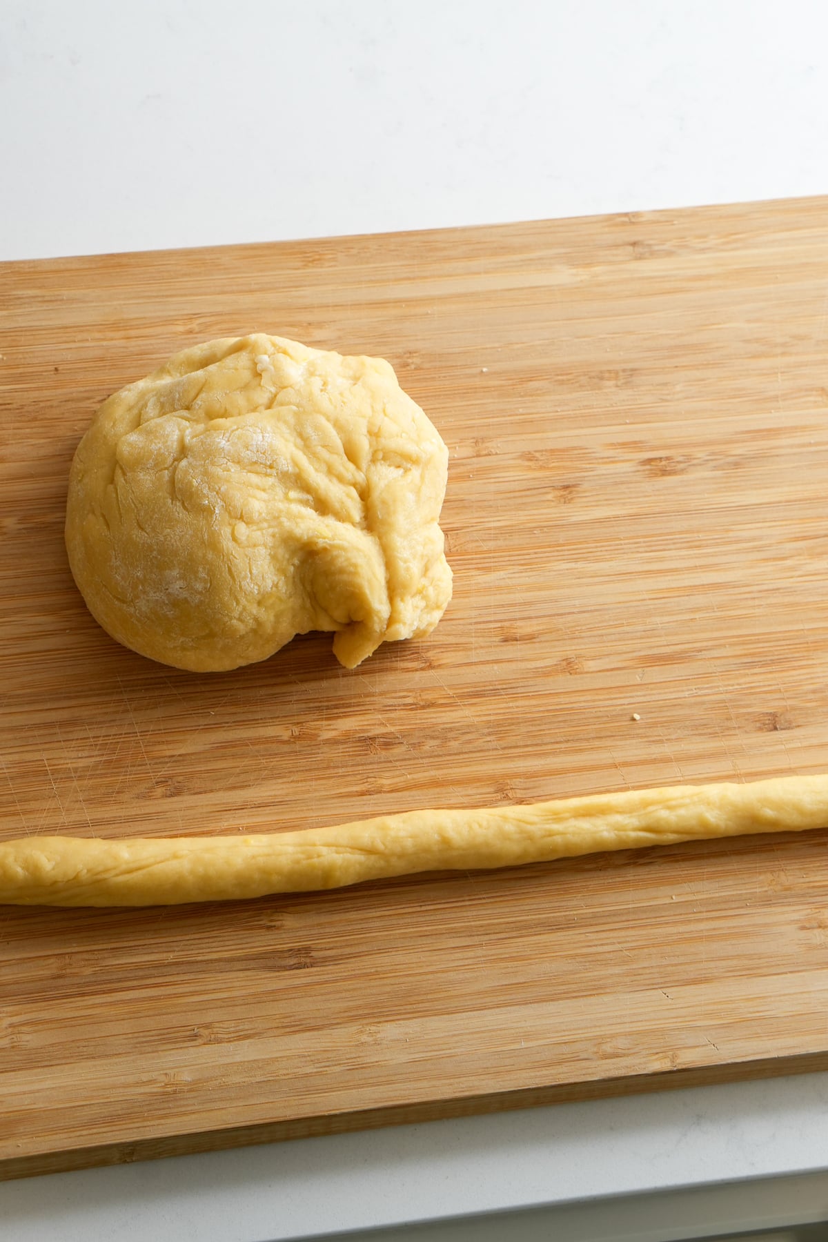 Ball of struffoli dough on a wooden board and a rope of dough