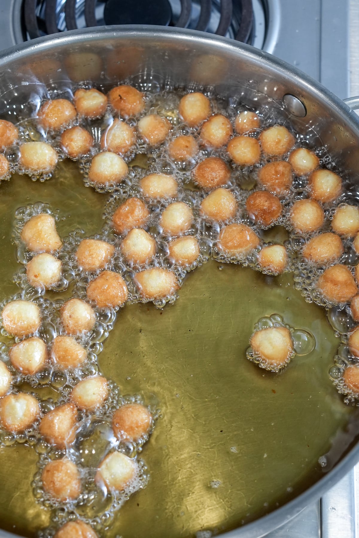 Struffoli being fried in oil in a large pan