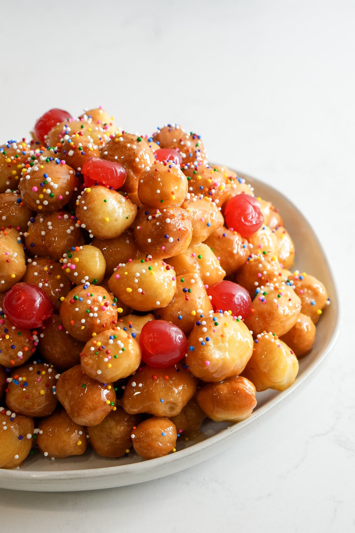 Mound of struffoli on a plate topped with sprinkles and maraschino cherries