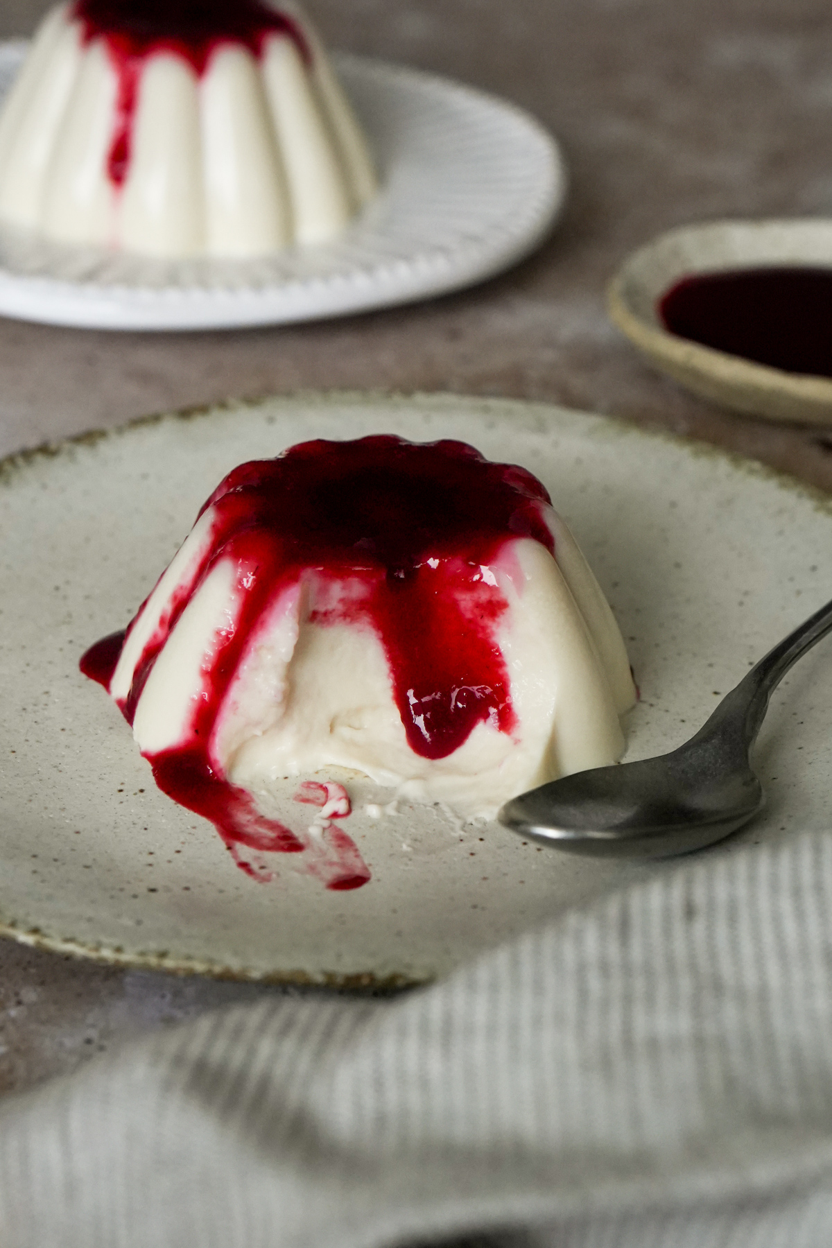 Panna cotta in a dish topped with raspberry coulis, with a spoonful removed