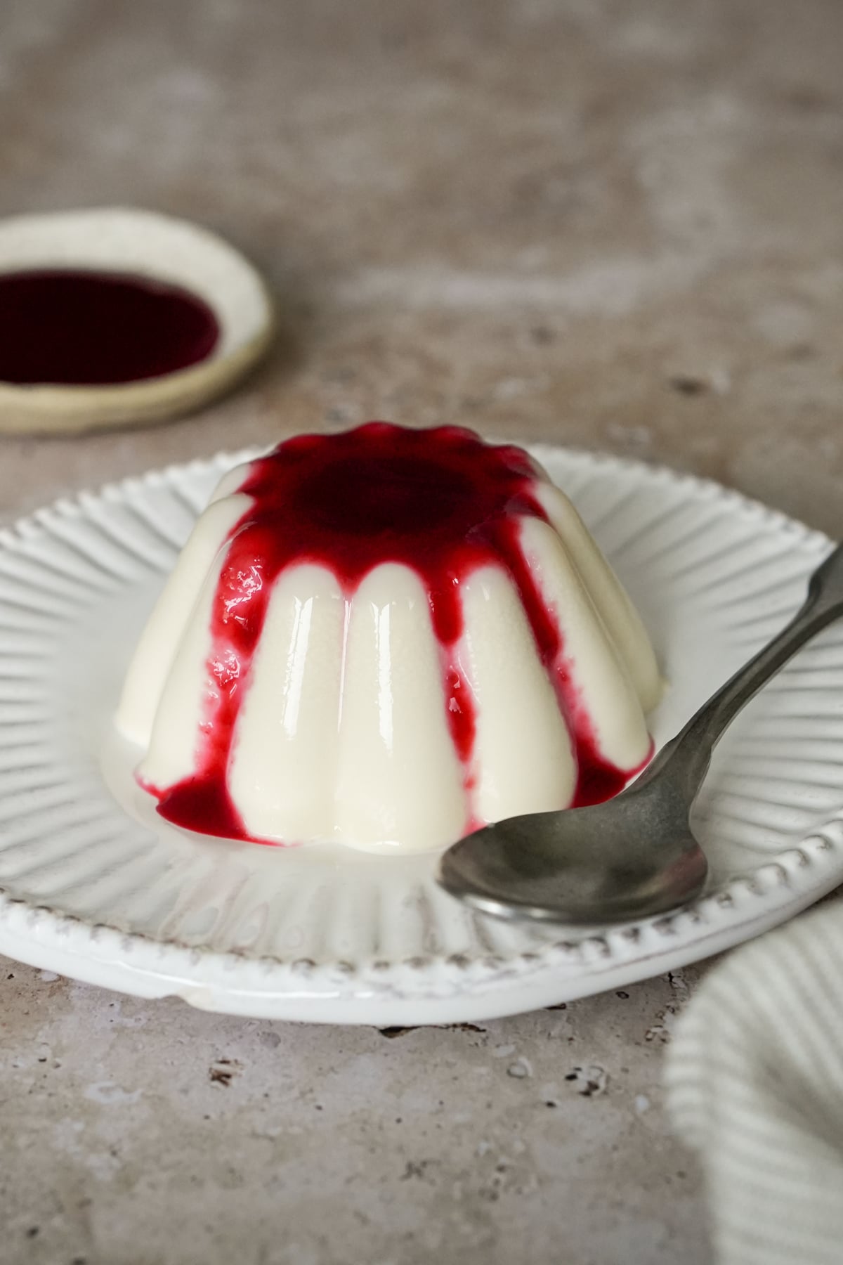 Panna cotta in a dish topped with raspberry sauce with a spoon to the side