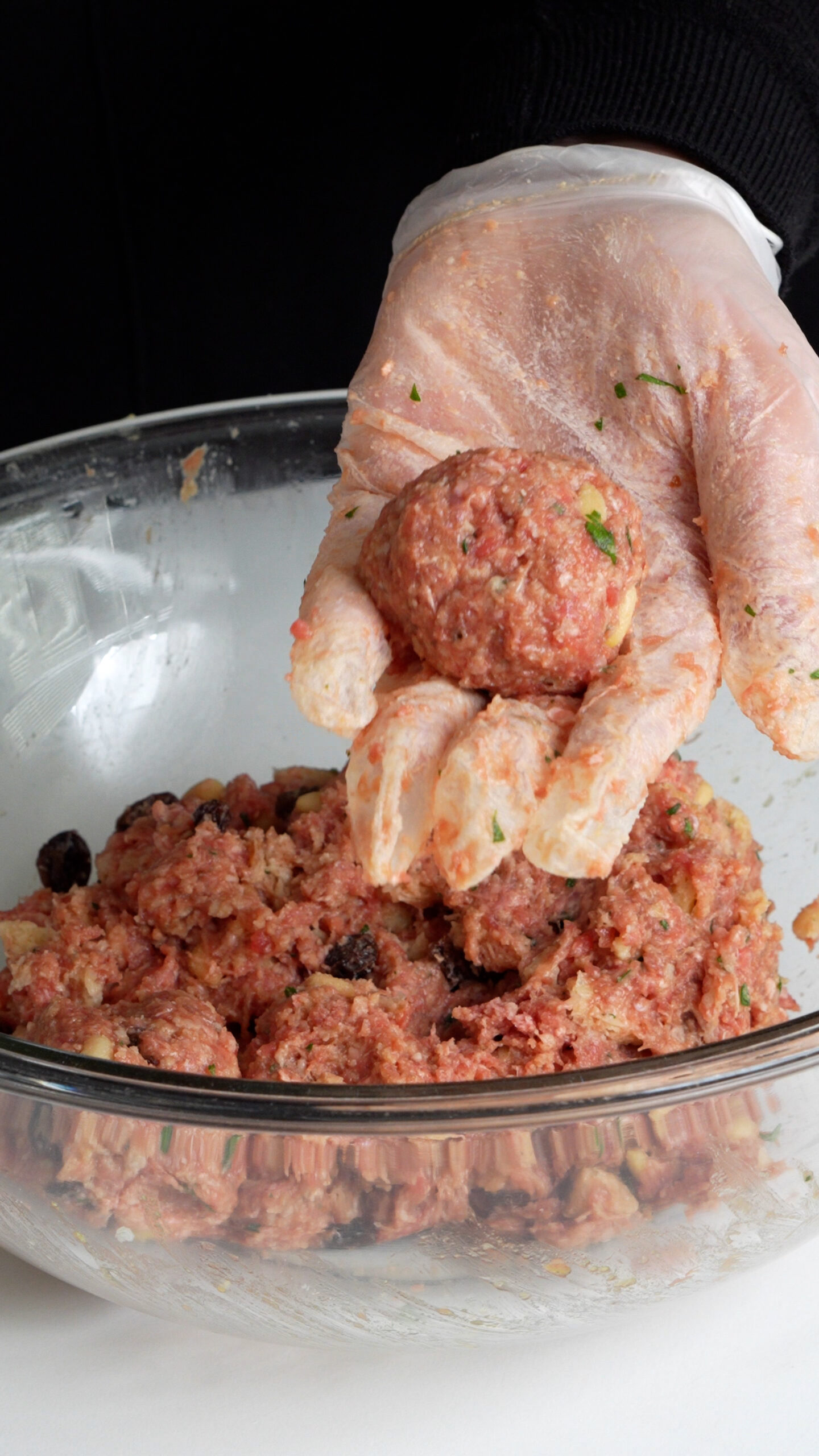 Raw meatball in palm of hand over a bowl with meatball filling