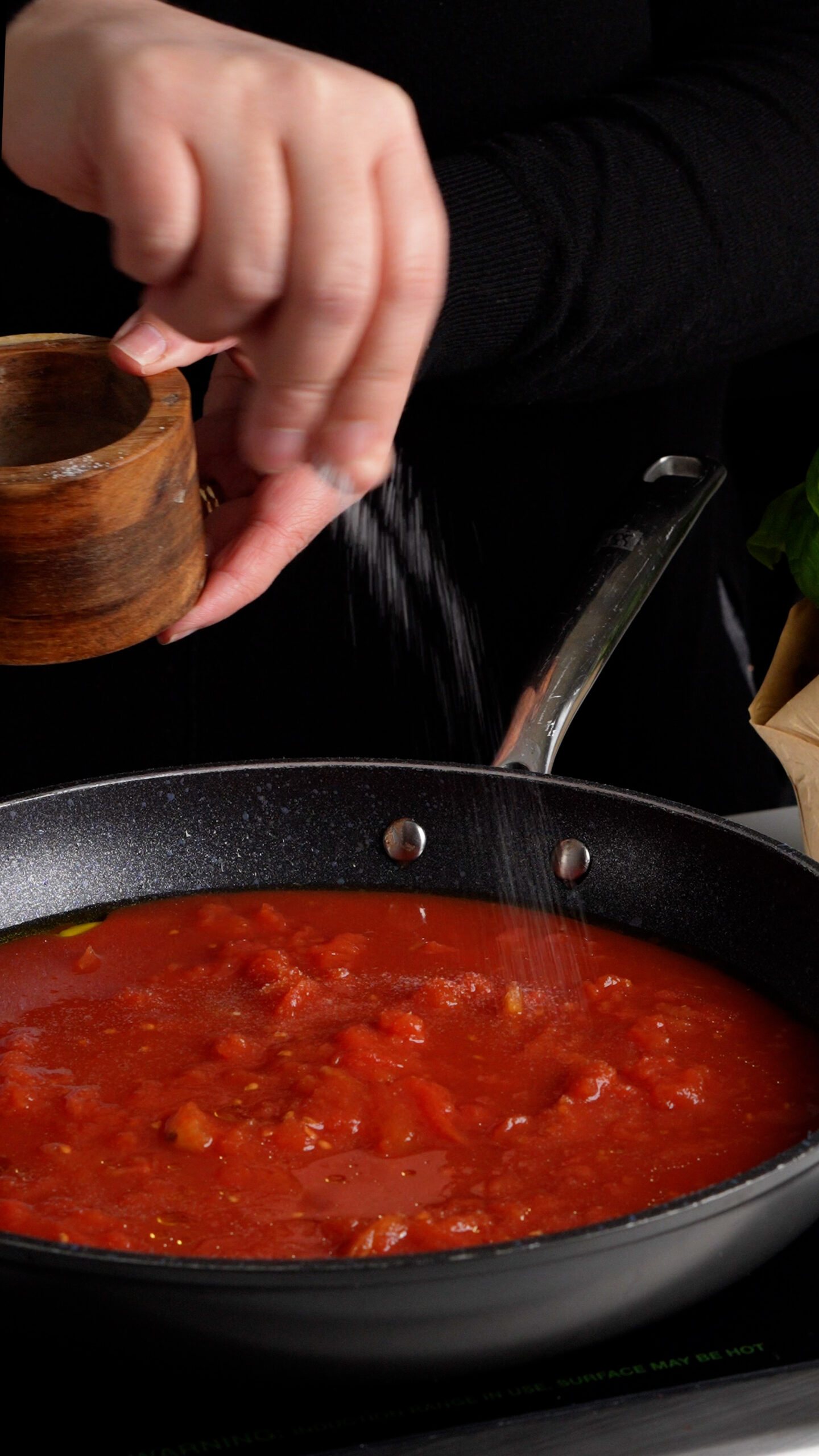 Pan with crushed tomatoes inside being salted