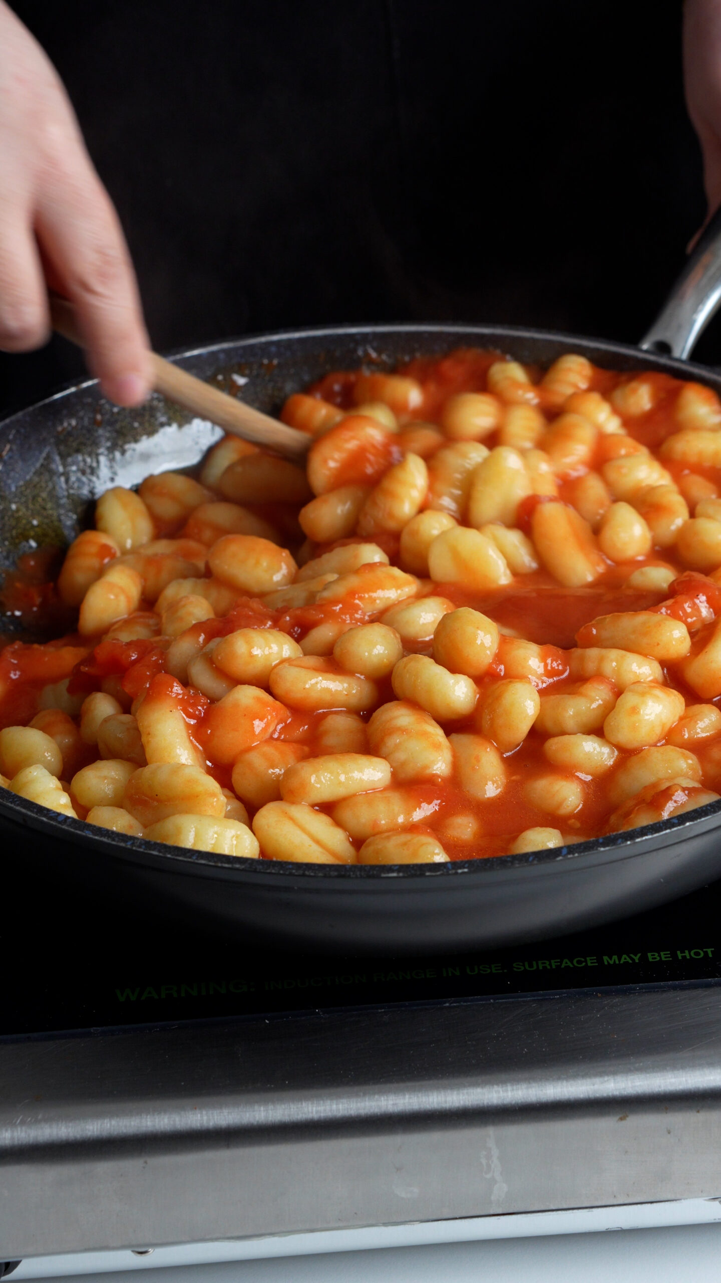 Gnocchi being mixed in a pan with tomato sauce