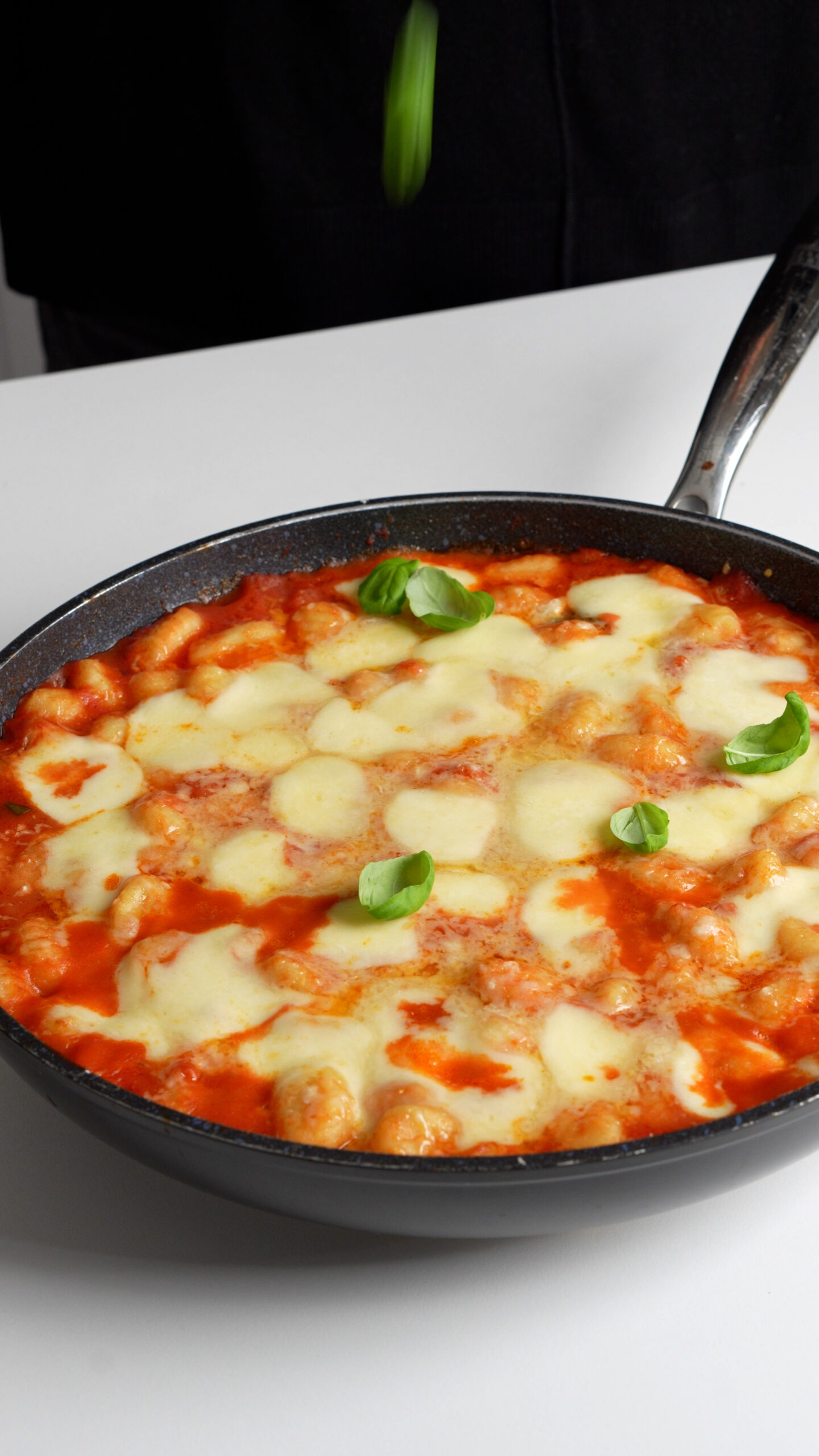 Baked gnocchi in a pan with melted mozzarella on top and fresh basil