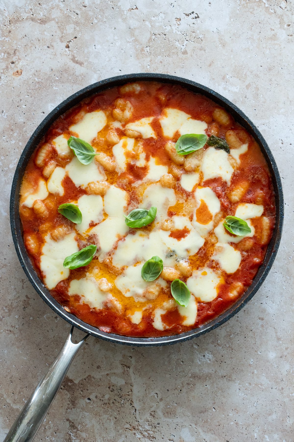 gnocchi in a pan with tomato sauce topped with melted mozzarella and fresh basil