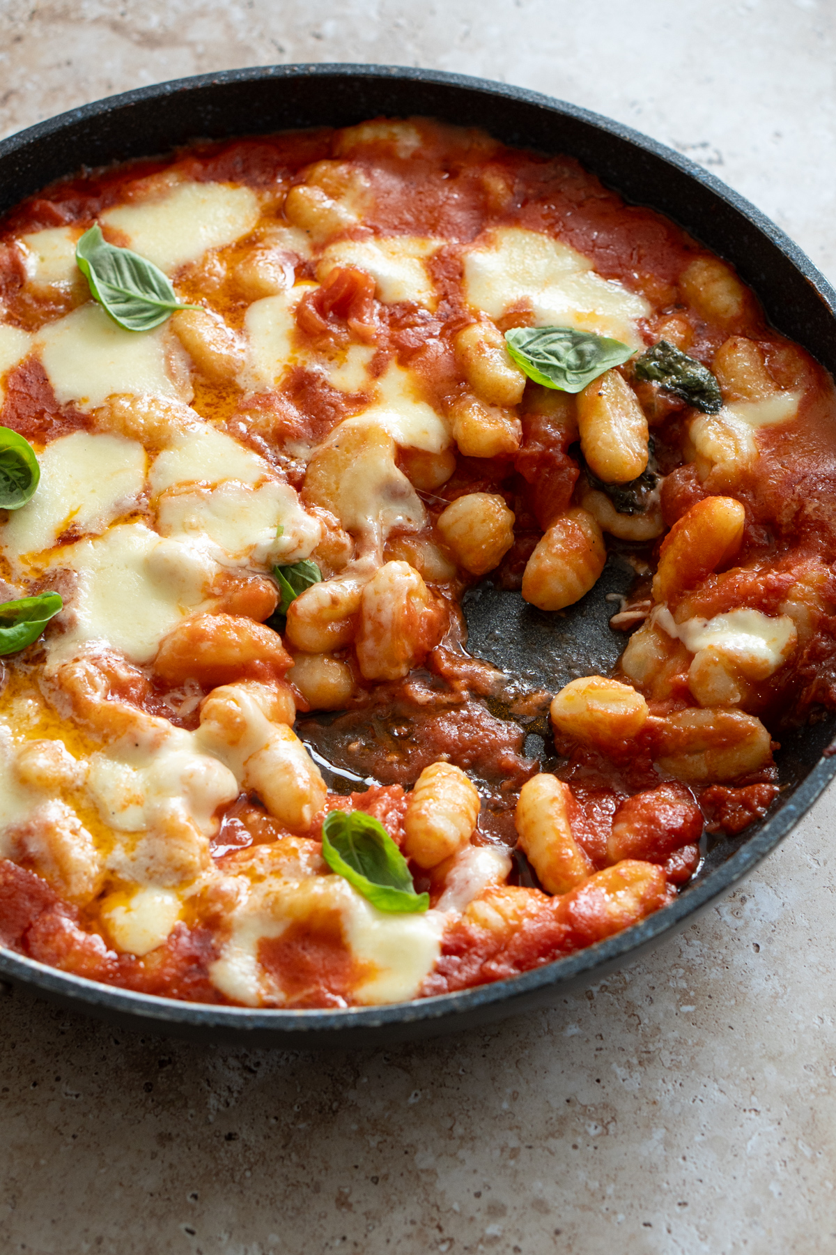 gnocchi in tomato sauce in a pan topped with melted mozzarella with a scoop taken out