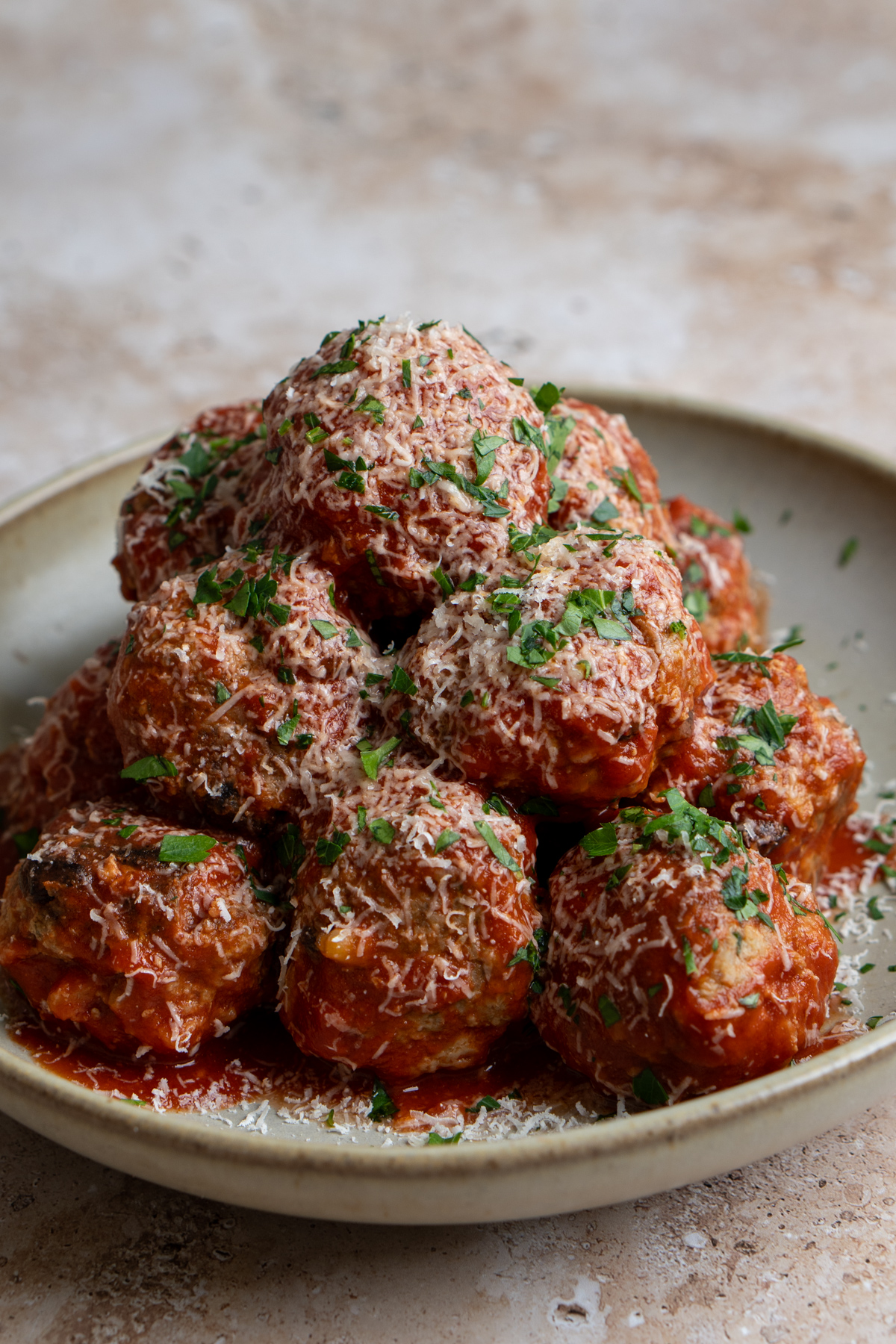 Meatballs piled high in a plate drenched in tomato sauce and sprinkled with grated parmigiano reggiano and minced parsley
