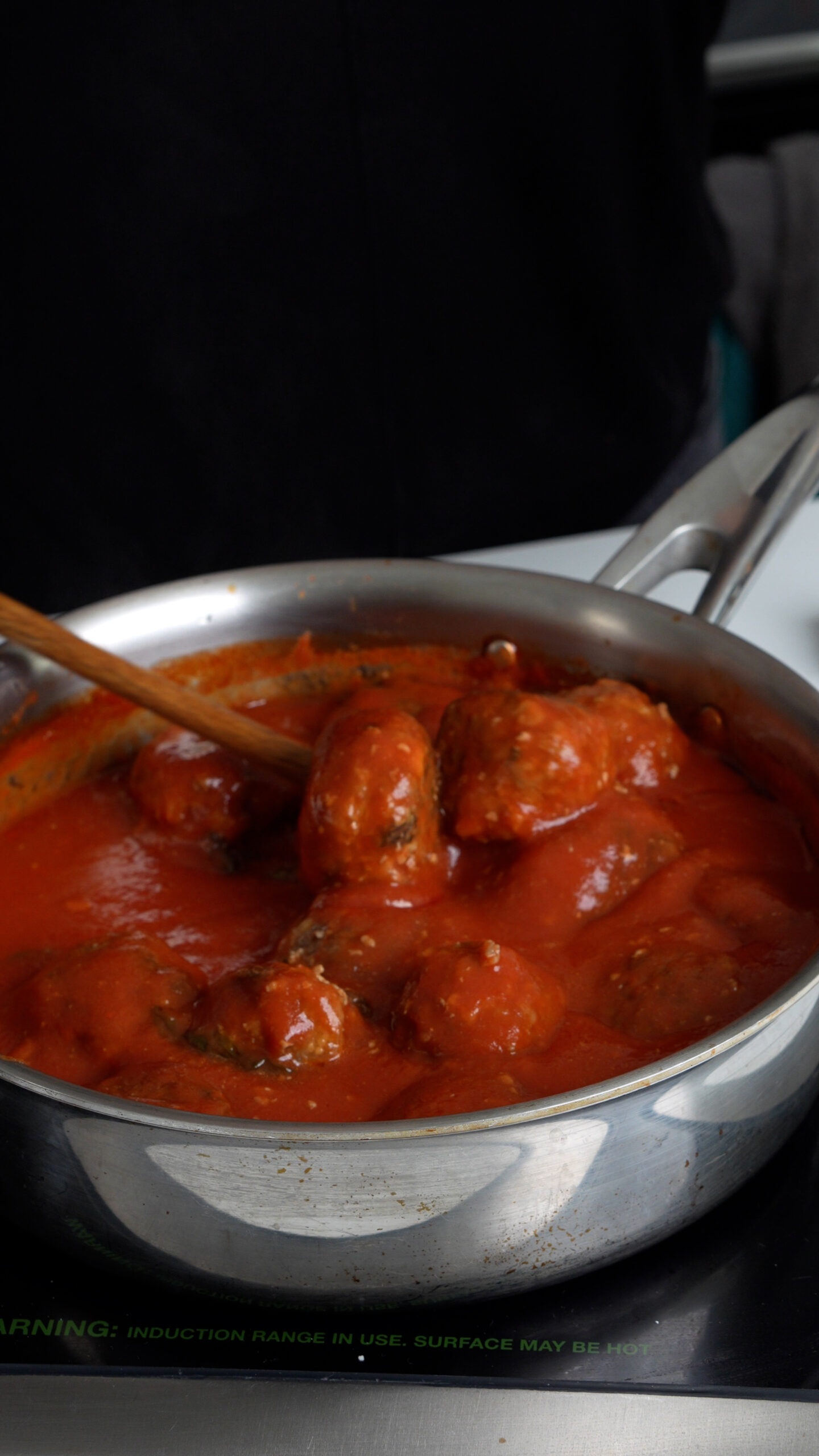 Meatballs being mixed in tomato sauce