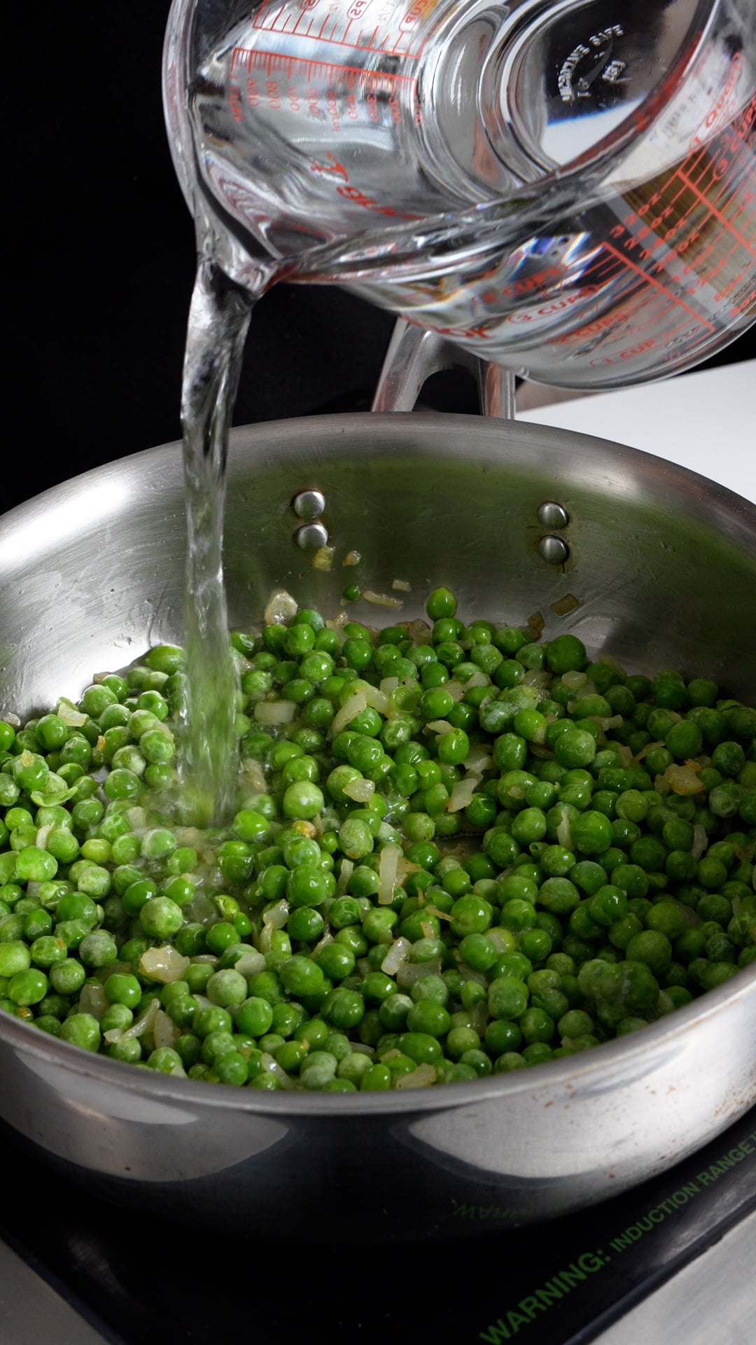 Peas and onions in a pan with water being poured in