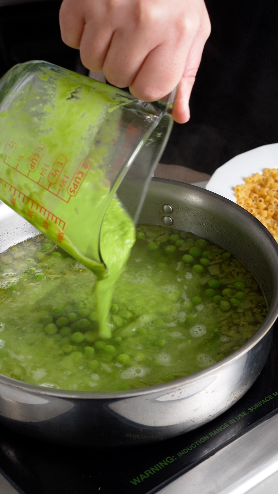 pea puree being poured into a pan with peas and water in it