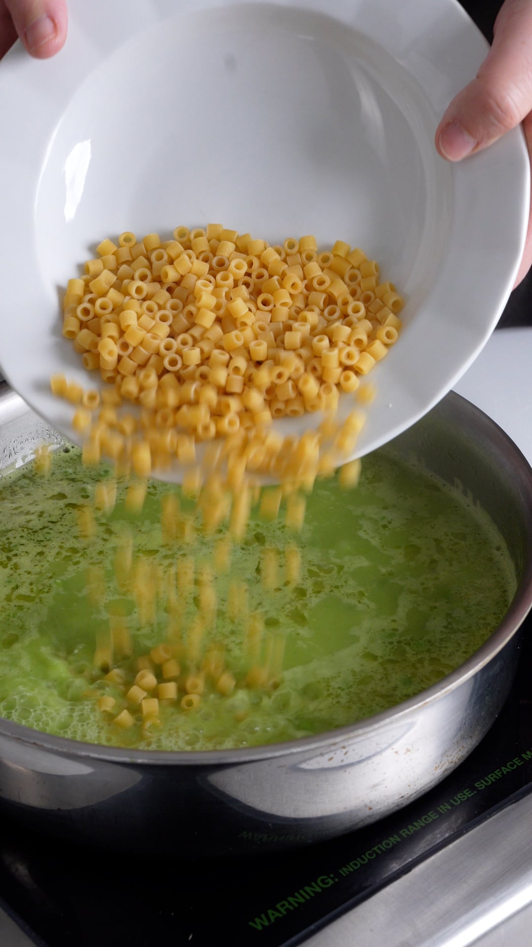 ditali pasta being added to a pan with peas and water in it