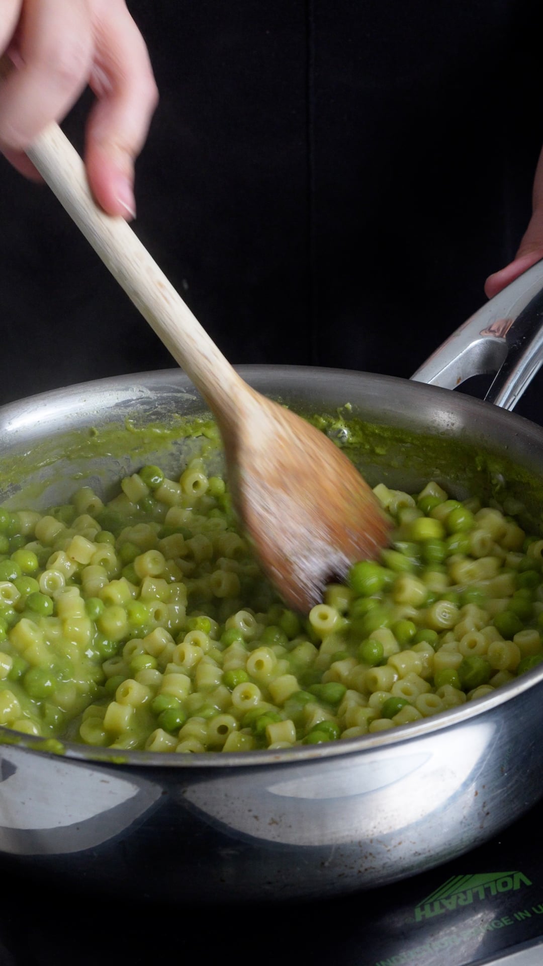 pasta e piselli being stirred in a pan with a wooden spoon