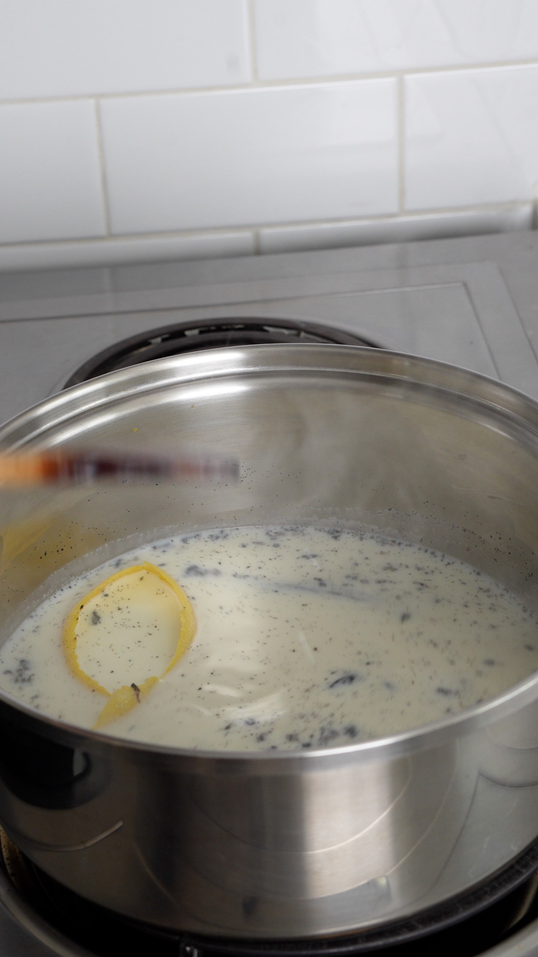 Milk, empty vanilla bean. vanilla bean seeds and lemon peel being heated up in sauce pan