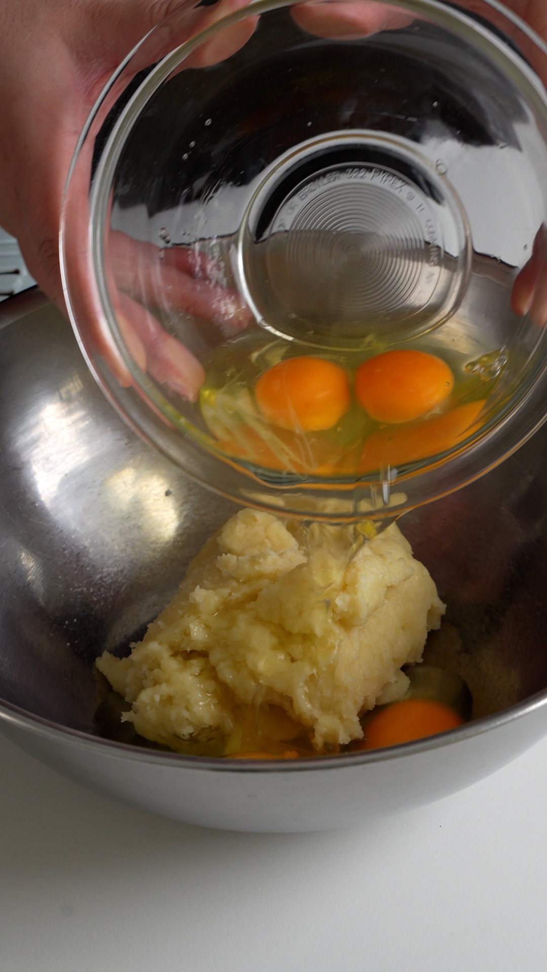 Ball of zeppole dough in a bowl with eggs being poured into it