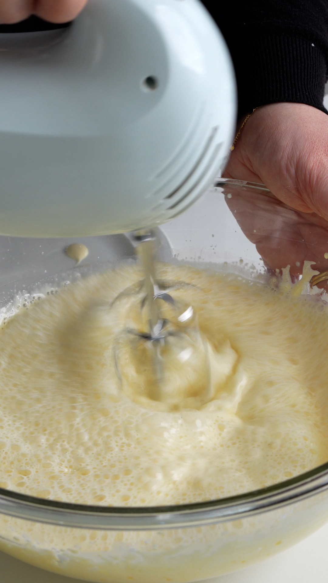 Milk, egg yolks, sugar and corn starch in a glass bowl being mixed with a hand mixer
